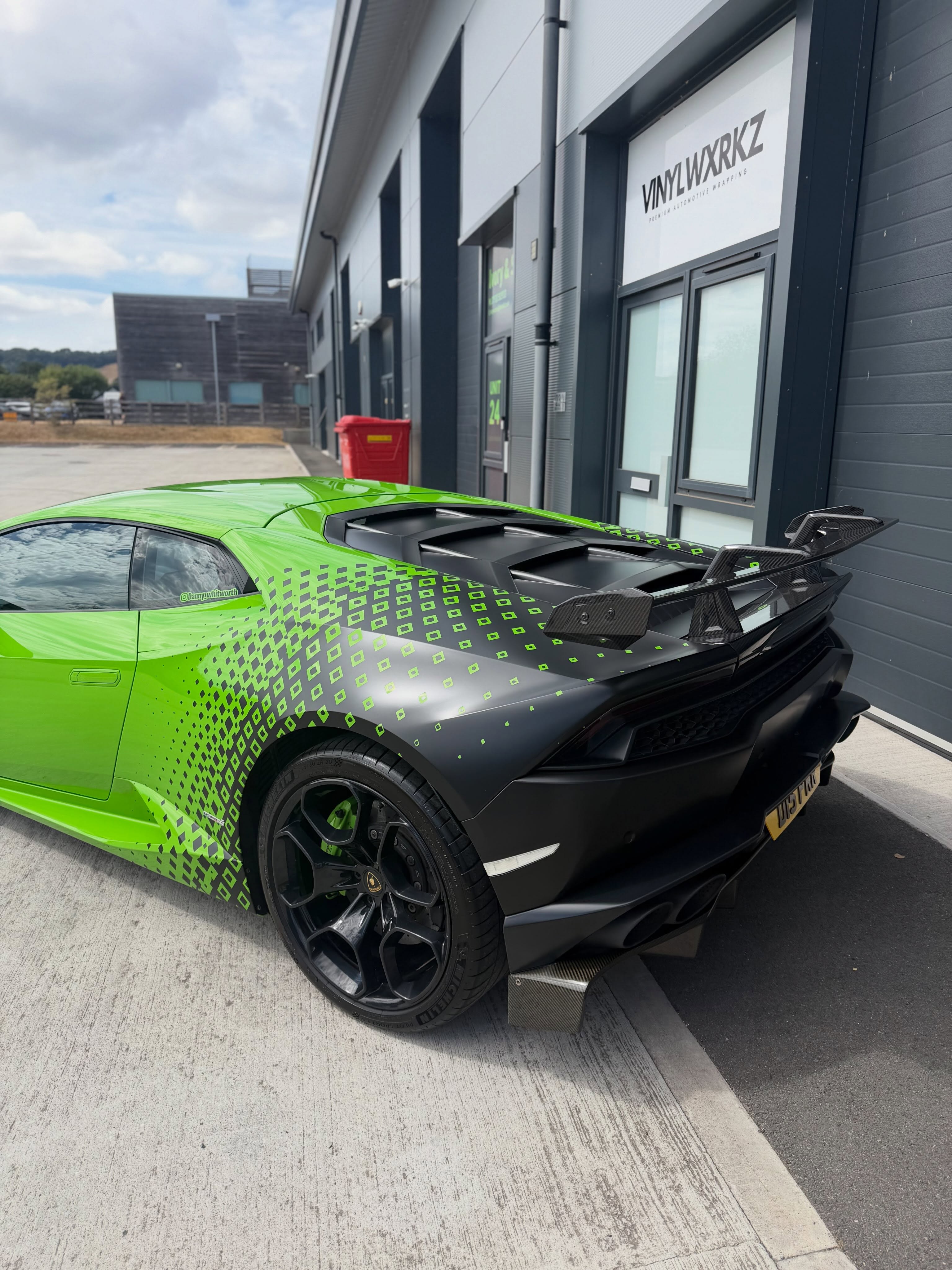 Rear three-quarter of the green Lamborghini Huracán with satin black and green diamond fade half-wrap and carbon spoiler